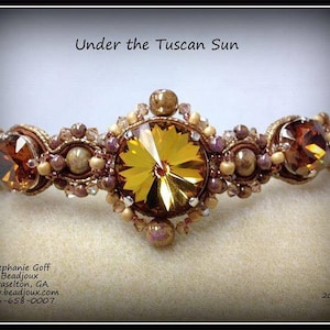 May include: A handcrafted beaded crown with the text "Under the Tuscan Sun." The crown features a large, faceted yellow-gold crystal center stone, flanked by smaller amber-colored crystals and various beads in shades of gold, brown, and purple.