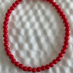 Puede incluir: Un collar de cuentas rojas con un diseño sencillo. Las cuentas son redondas y lisas, y el collar está enhebrado en un hilo transparente.