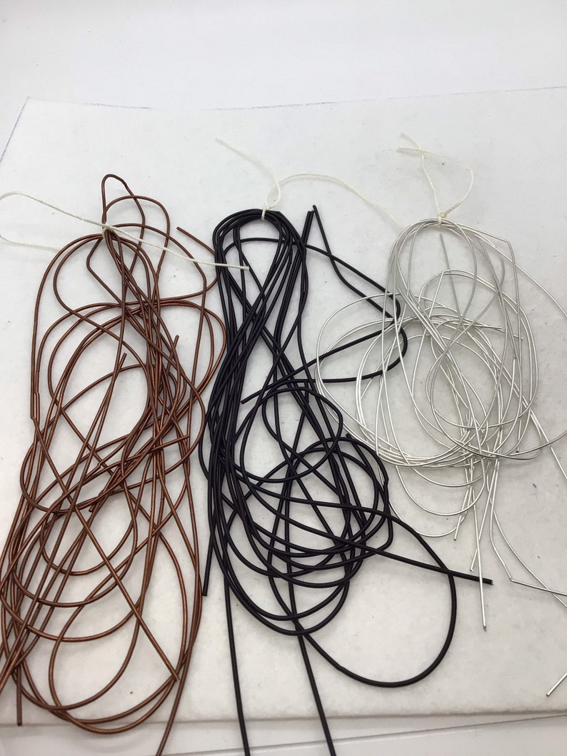 May include: Three bundles of thin, flexible wire in copper, black, and silver colors. Each bundle is loosely coiled and secured with a thin white string, creating a tangled appearance with multiple individual wire strands visible in each color group.