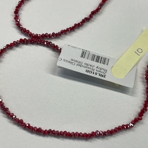 May include: A strand of red glass beads with a shiny finish. The beads are small and round, and they are strung on a clear thread. The beads are labeled "2mm Roundel Glass Ruby Jade Shine Made in China".