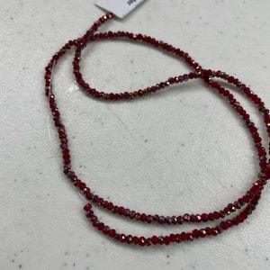 May include: A strand of red crystal beads with an iridescent finish. The beads are strung on a clear thread. The label reads "Thunder Polish Glass Crystal".