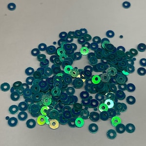 Może przedstawiać: Stosik turkusowych, opalizujących cekinów w kształcie kół.