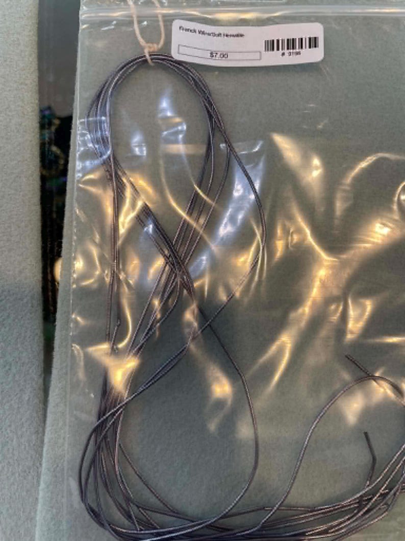 May include: A bundle of thin, metallic silver-toned French wire or gimp cord contained within a clear plastic zip-top bag. The bag features a white adhesive label with the text French Wire/Soft Hevielle and a barcode printed on the surface.