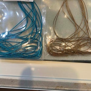 May include: Two clear plastic bags containing French wire, one with bright sea blue wire and the other with bronze wire. Each bag features a white label with text reading French Wire/Soft Sea Blue and French Wire/Soft Silk Bronze respectively.