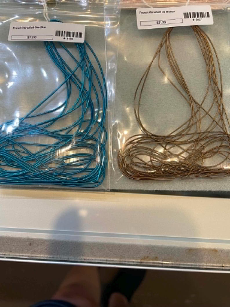 May include: Two clear plastic bags containing French wire, one with bright sea blue wire and the other with bronze wire. Each bag features a white label with text reading French Wire/Soft Sea Blue and French Wire/Soft Silk Bronze respectively.