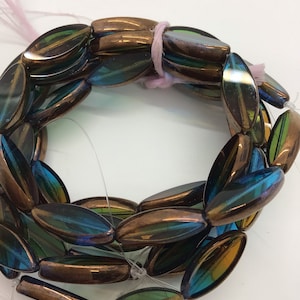 Op de afbeelding: Een streng iriserende glazen kralen in tinten groen, blauw en koper. De kralen zijn ovaalvormig en hebben een glanzende afwerking.