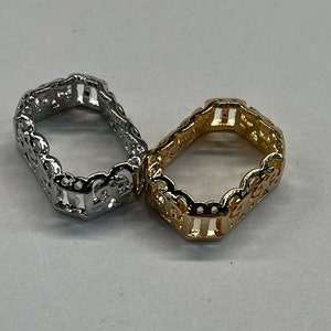 May include: Two rings, one silver and one gold, with an intricate, openwork design. The rings are both square shaped and have a delicate, ornate pattern.
