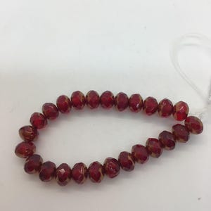 Può includere: Una collana di perline di vetro rosse con un luccichio dorato. Le perline sono sfaccettate e hanno una forma rotonda.