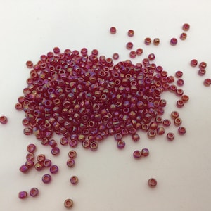 May include: A large pile of small, iridescent red glass beads. The beads are round and have a metallic sheen.