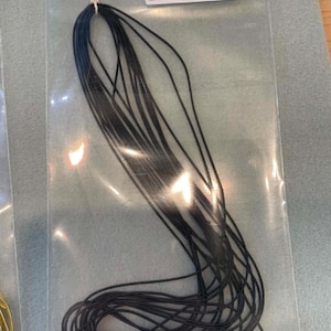 May include: A bundle of thin, black, flexible cord material packaged in a clear plastic bag. The bag features a white adhesive label at the top with the text "French Wire/Gimp Matte Black" and a barcode, along with a small white string loop.