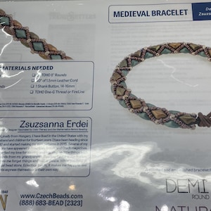 May include: A close-up of a beaded bracelet with a medieval design. The bracelet is made with brown, green, and gold beads. The bracelet is stitched and embellished with a demi-round matludo bead. The bracelet is designed by Zsuzsanna Erdei.