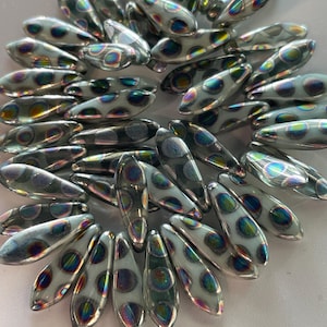 May include: A collection of iridescent glass beads with a white and gray polka dot pattern. The beads are shaped like teardrops and have a slightly curved shape.