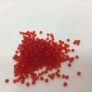 Peut inclure: Un tas de petites perles de verre orange. Les perles sont rondes et légèrement translucides.