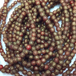 May include: A strand of red glass beads with a gold glitter finish. The beads are round and have a textured surface.