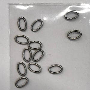 May include: A close-up of a bag of silver oval jump rings. The jump rings are about 1/2 inch in diameter.