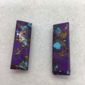 Puede incluir: Dos piezas rectangulares de piedra con patrones de color púrpura, azul y dorado. Las piedras tienen una textura rugosa y natural.