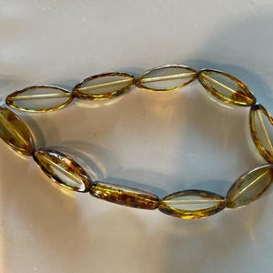 Op de afbeelding: Een streng ovale, doorschijnende amber kralen met bruine en gouden vlekken.