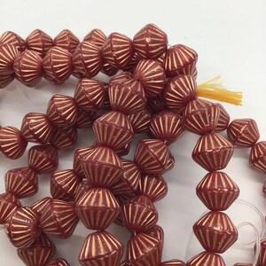 Op de afbeelding: Een streng rode glazen kralen met een gouden metallic afwerking. De kralen zijn gefacetteerd en hebben een stervormig ontwerp.