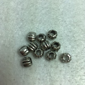 Könnte beinhalten: Eine Gruppe silberner Metallperlen mit einem geriffelten Design. Die Perlen haben ein kleines Loch in der Mitte zum Auf fädeln.