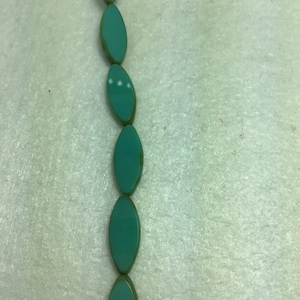 Op de afbeelding: Een streng turquoise ovale kralen met een groene rand.