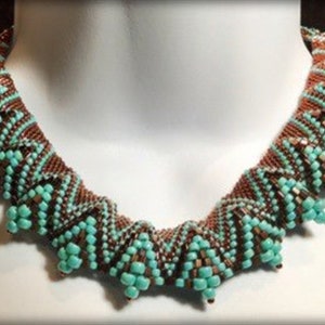 Op de afbeelding: Een turquoise en bruine kralenketting met een geometrisch patroon. De ketting is gemaakt van kleine kralen en heeft een uniek, ingewikkeld ontwerp.