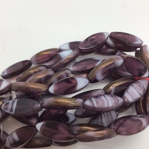 Op de afbeelding: Een streng paarse en witte glazen kralen met een metallic glans. De kralen zijn ovaalvormig en hebben een swirl-patroon.