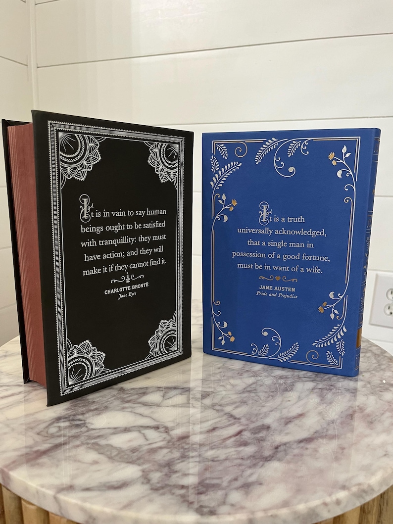 May include: Two hardcover books with decorative covers. The book on the left has a black cover with silver floral designs and the text "It is in vain to say human beings ought to be satisfied with tranquillity: they must have action; and they will make it if they cannot find it."  The book on the right has a blue cover with silver floral designs and the text "It is a truth universally acknowledged, that a single man in possession of a good fortune, must be in want of a wife."