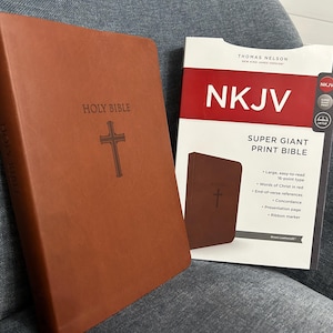 May include: A brown leather-bound New King James Version (NKJV) Holy Bible with a cross embossed on the cover. The bible is next to a product description card for a super giant print NKJV bible.