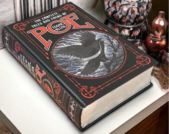 May include: A black hardcover book with a red and gold design. The book is titled "The Complete Tales and Poems of Edgar Allan Poe" and features a black raven with the words "Nevermore" on a banner.