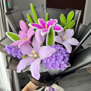 May include: A bouquet of artificial flowers in shades of pink, purple, and green, wrapped in black paper. The bouquet includes lilies, hydrangeas, and other floral elements. A ribbon with the text "JUST FOR YOU" is tied around the base.