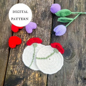 Puede incluir: Patrón de crochet para dos posavasos blancos con flores de amapola rojas y tallos verdes. El patrón está disponible para descargar digitalmente. La imagen también muestra una variedad de flores de crochet en morado y rojo.