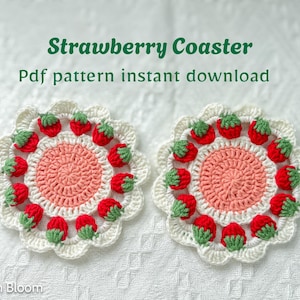 Puede incluir: Dos posavasos de fresa hechos a mano con ganchillo. Cada posavasos presenta un círculo central rosa rodeado de fresas rojas con copas verdes y un borde festoneado blanco. El texto dice "Strawberry Coaster" y "Pdf pattern instant download".