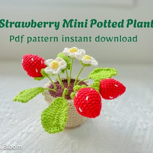 May include: A crocheted strawberry mini potted plant with red strawberries, white flowers, and green leaves. The plant is in a small beige pot. Text on the image reads "Strawberry Mini Potted Plant" and "Pdf pattern instant download".