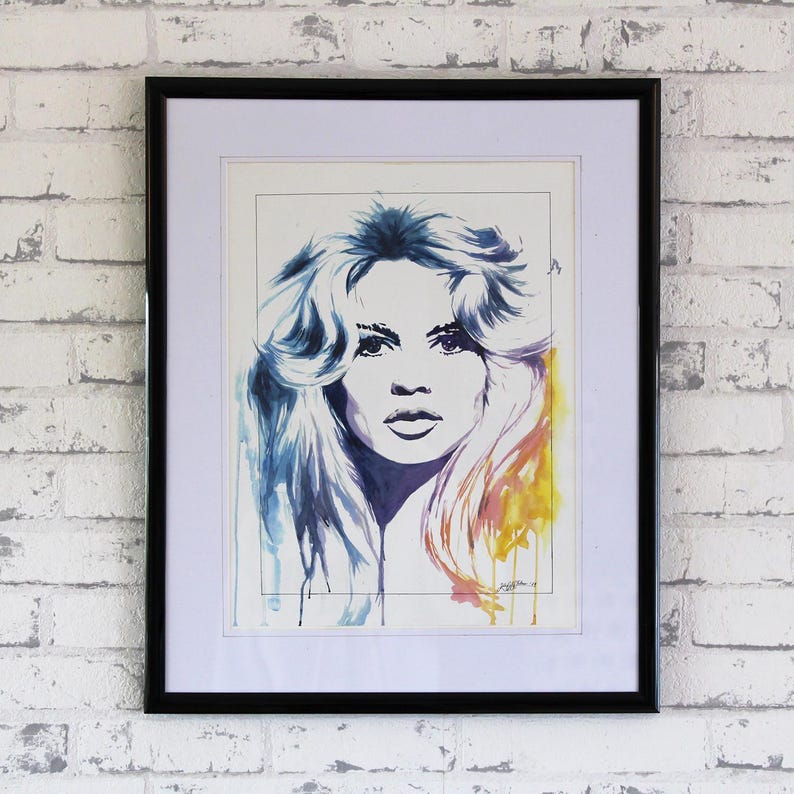 Peut inclure: Un portrait encadr&eacute; &agrave; l'aquarelle d'une femme aux longs cheveux flottants. L'&oelig;uvre pr&eacute;sente une palette de couleurs de bleus, de jaunes et d'oranges, avec le visage du sujet dans un ton neutre. L'&oelig;uvre est encadr&eacute;e dans un cadre noir.