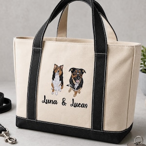 May include: A cream-colored canvas tote bag with black handles and a black base. The front features embroidered illustrations of two dogs and the text "Luna & Lucas" in black script. The bag has a structured rectangular shape with top handles.