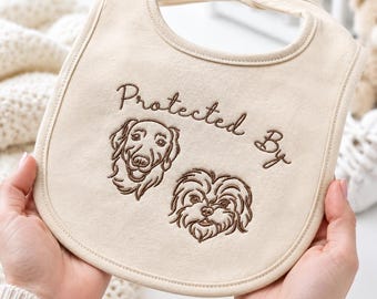 Peut inclure: Un bavoir pour bébé de couleur crème avec une broderie marron représentant deux têtes de chien et le texte "Protected By" centré au-dessus. Le bavoir est de forme arrondie avec une fermeture à pression et des bords cousus.