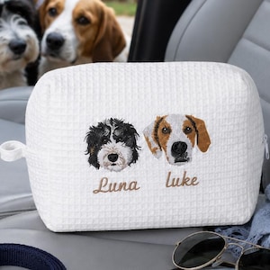 May include: A white waffle-textured fabric pouch featuring embroidered portraits of two dogs. The left dog is black and white, labeled with the name Luna, and the right dog is brown and white, labeled with the name Luke, both in brown thread.