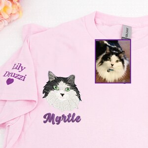 Personalized embroidered cat shirt in light pink featuring a custom pet portrait of a white flame-point cat with blue eyes named Myrtle. Unique embroidery includes the cat’s face on the front and name on the sleeve in purple thread with heart detail. Custom gift for cat moms, pet lovers, and memorial keepsakes.