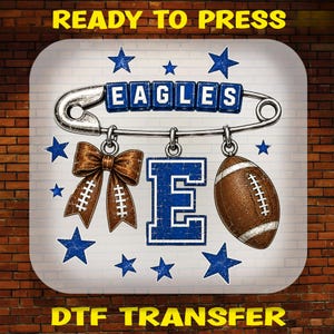 May include: A DTF transfer design featuring a large silver safety pin with blue letter blocks spelling EAGLES. Hanging from the pin are a brown bow with white laces, a large blue letter E, and a brown football. Blue stars surround the elements.