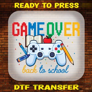 May include: A DTF transfer design featuring the pixelated text GAME OVER in red, blue, green, and yellow. Below, a white game controller is surrounded by an open book, a red apple, a blue crayon, and a yellow pencil, with back to school text.