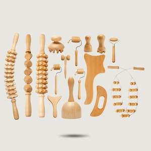 Può includere: Una collezione di strumenti per massaggi in legno chiaro che include vari rulli con ruote testurizzate, una coppa a forma di campana, una tavola da raschiamento curva, un massaggiatore manuale con manico e un rullo a corda flessibile con perline in legno.