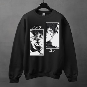 May include: Black sweatshirt featuring a manga-style graphic. The design is split into two white rectangular panels, each displaying a character's face. Japanese text is above each character. The sweatshirt is hanging on a black hanger.