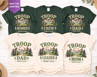 May include: A collection of six short-sleeve t-shirts in dark green and cream colors. Each shirt features a graphic of mountains, pine trees, and a sun, with the text TROOP, the specific role like MEMBER, CREW, DAD, LEADER, or MOM, and TROOP 12345.
