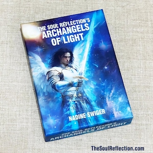 May include: A blue and white oracle card deck box with the title "The Soul Reflection's Archangels of Light" and the author's name "Nadine Swiger". The box features an illustration of an angel with wings and a sword.