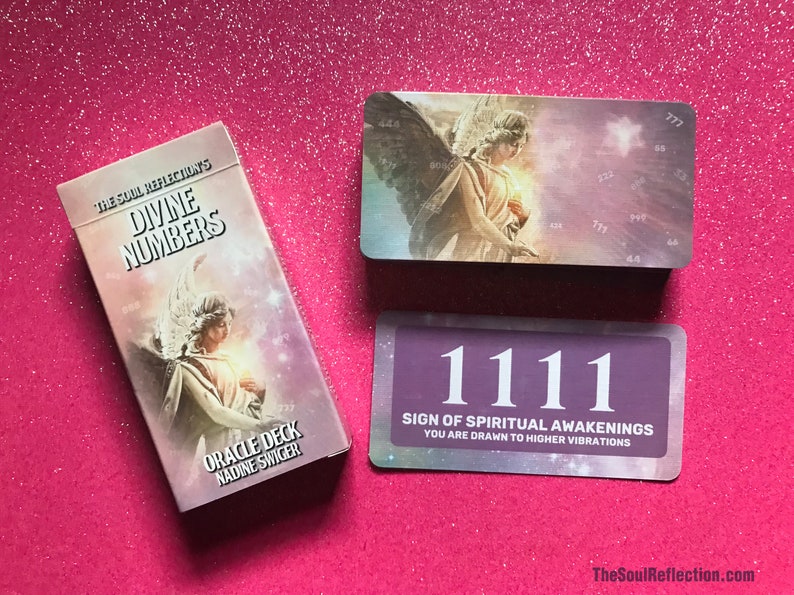 May include: A deck of "Divine Numbers" oracle cards with an angel illustration on the box and cards. One card displays the number "1111" with text "Sign of Spiritual Awakenings". The deck is on a pink glitter surface.