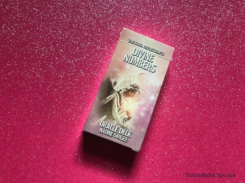 May include: A rectangular oracle deck titled "Divine Numbers" by Nadine Swiger, featuring an angel illustration. The deck is set against a sparkly pink background. The text "The Soul Reflection's" is at the top.