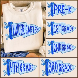 May include: A cream-colored crewneck sweatshirt featuring a blue pennant graphic with a gingham pattern and a blue ribbon. The pennant displays the text KINDER GARTEN. Additional pennant designs show PRE-K, 1ST GRADE, 2ND GRADE, 3RD GRADE, and 4TH GRADE.