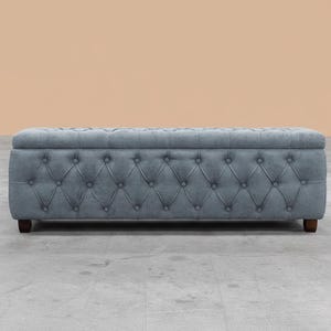 May include: A blue storage bench with a tufted diamond pattern. The rectangular bench has wooden legs and a hinged top. The colour is a muted blue-grey. The bench is approximately 150 cm long, offering a stylish storage solution.