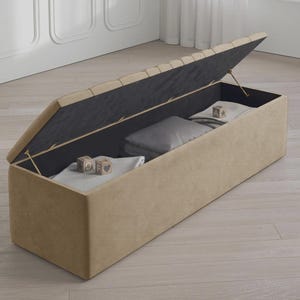 May include: A beige rectangular storage bench with a hinged lid, partially open to reveal folded blankets and pillows. The interior is black, and the lid's top has a tufted design. Wooden blocks with letters and symbols are inside.