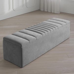May include: A gray upholstered storage bench with a rectangular shape. The bench features a padded, ribbed top and a solid base. The neutral color and simple design make it suitable for various interior styles. The bench is approximately 60 inches long.